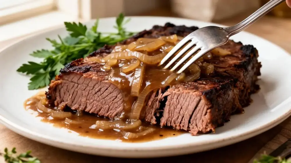 Fork pulling apart a tender slice of braised brisket topped with onion gravy on a white plate