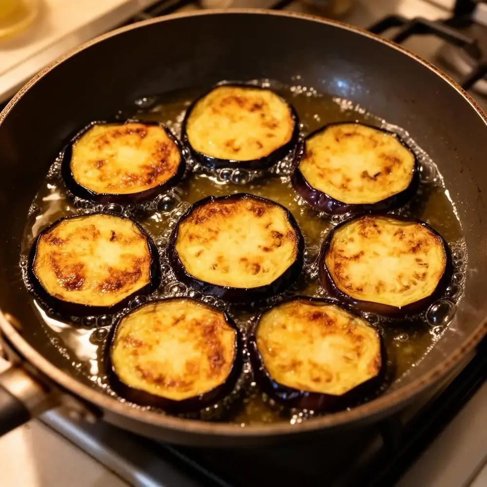 Eggplant slices frying to golden brown in a skillet of hot oil